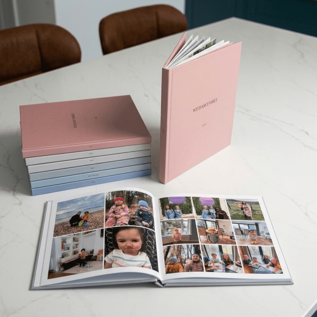 A stack of hardcover yearbooks in a range of cover colours, one standing with the family name and year on the front, and another lying open to show printed photo pages