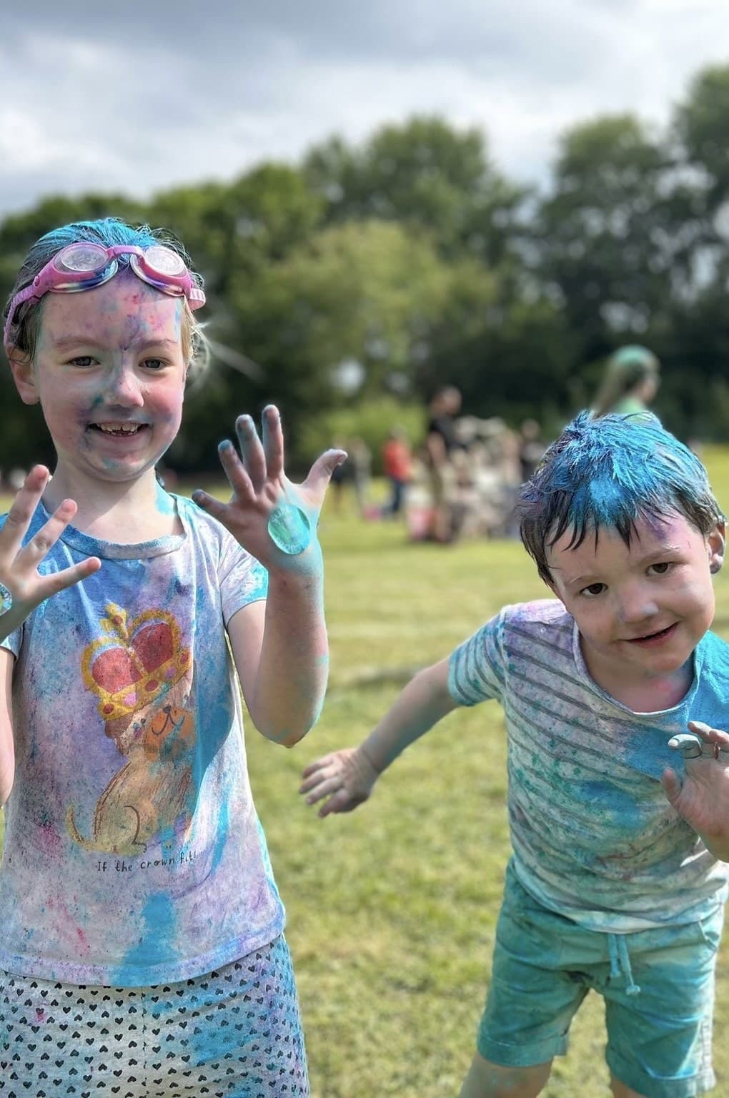 Two children covered in coloured powder at a school colour run, holding up their painted hands